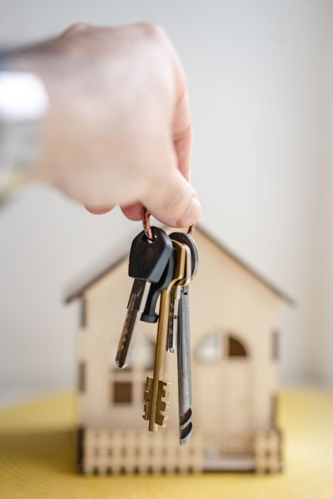 A person hold keys up with a mini model home in the background