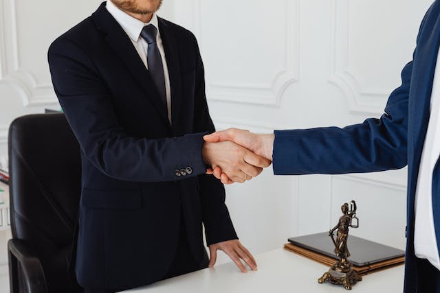 a landlord shaking hands with someone across a desk with a statue of lady justice between them