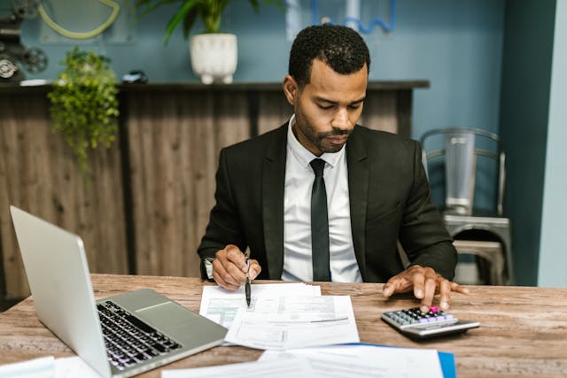 person sitting a desk using a calculator whole looking over documents