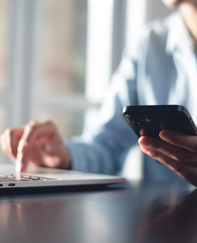 Guy on a laptop while also holding his phone