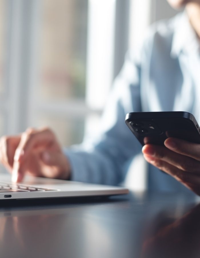 Guy on a laptop while also holding his phone